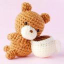 コーヒーカップにもたれる茶色のクマのあみぐるみ